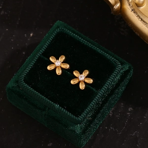 Gros plan d'une boucle d'oreille fleur en or avec zircon dans un écrin en velours vert