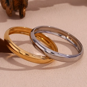 Close-up of interlocking gold and silver polished stainless steel bangles on pink surface