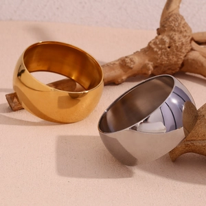 Polished gold and silver wide arc bangles displayed on a minimalist natural background
