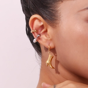 Close-up of 18K gold cowboy boot earrings, diamond ear cuff and pearl clip on a model