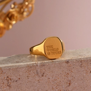 Vista macro de anillo de sello dorado con grabado THE WORLD IS YOURS en cara pulida