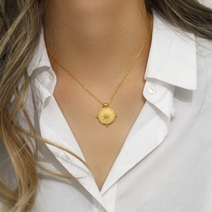 Gros plan du collier boussole solaire en or 18K porté sur un élégant chemisier blanc