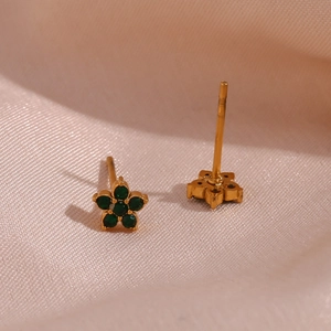 Close-up of 18K gold plated flower earrings with green zircon on pink satin cloth