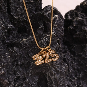 Detail of gold snake chain with crystal-encrusted numbers 1, 2, and 5 on black volcanic rock