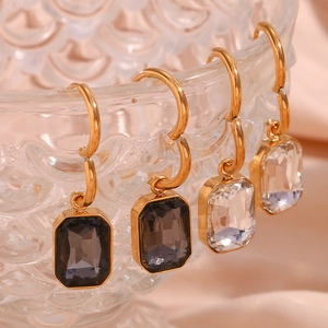 Close-up of gold rectangle earrings with clear and grey crystals on a glass edge