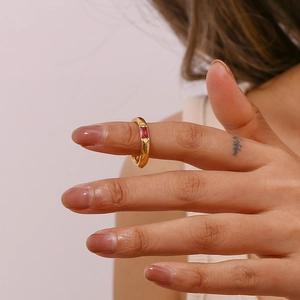 Dettaglio di un anello in acciaio dorato con zircone rosso rettangolare indossato