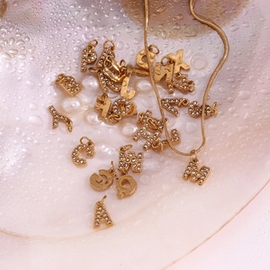 Detail of 18K gold plated letter pendants with zircons on a snake chain over shell tray