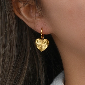 Macro view of gold heart earrings with sunburst texture worn on a model ear