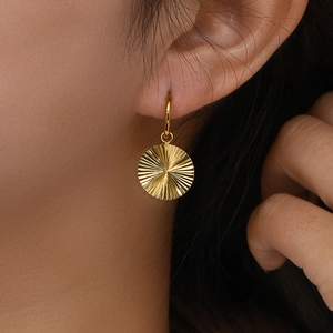 Detailed view of gold hoop earrings with sunburst textured disc pendants on a model