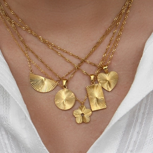 Macro detail of gold-plated geometric necklaces with sunburst textures on white shirt