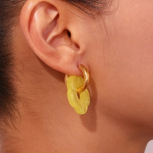 Close-up of model wearing gold hoop earrings with yellow translucent wavy flower pendants