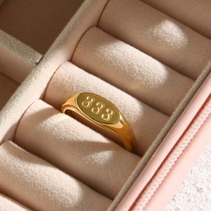 Primo piano di anello a sigillo ovale placcato oro con numero 333 inciso in una scatola