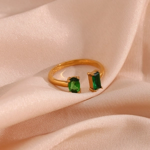Macro d'une bague ouverte dorée ornée de zircons ovales et rectangulaires vert émeraude