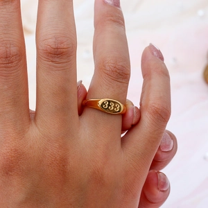 Primo piano di un anello ovale dorato con incisione 333 al dito, stile retrò minimalista