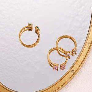 Détail de bagues dorées ornées de zircons émeraude, rose et cristal transparent