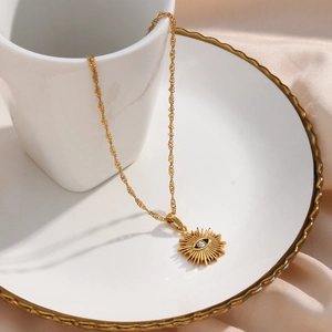 Macro detail of gold sunburst evil eye pendant with sparkling crystal on a water wave chain
