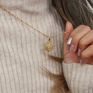Close-up of golden evil eye sunburst pendant with crystal on beige knit sweater