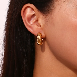 Detail of 18K gold plated C-shaped earrings with hollow heart pattern on model's ear