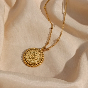 Close-up of 18K gold starburst pendant necklace resting on beige silk fabric