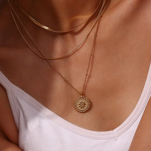 Detail of layered gold necklaces with starburst coin pendant on a female model