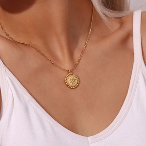 Detail of 18K gold starburst disc pendant necklace on white V-neck attire
