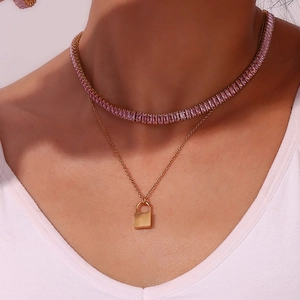 Detail van een dubbellaagse 18K vergulde ketting met roze zirkoon en slotvormige hanger