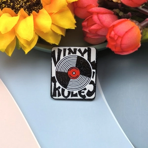 Macro view of a square vinyl record enamel pin with Vinyl Rules text and glitter finish