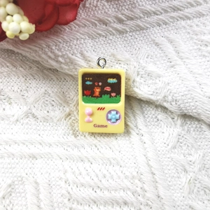 Macro shot of a yellow resin game console charm with silver hook on white knit fabric