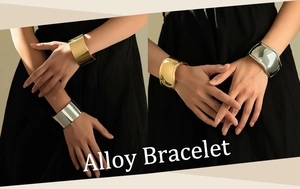 Close-up of chunky gold and silver alloy cuff bracelets with wavy irregular edges