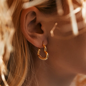 Elegant 18K gold plated heart earrings with textured design worn by a female model