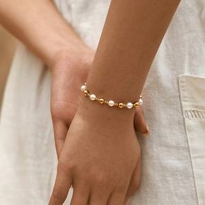 Elegante bracciale con perle bianche e sfere dorate indossato da una modella femminile