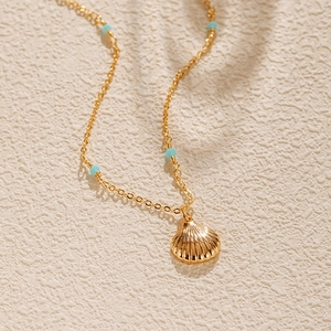 Détail d'un collier coquillage plaqué or avec perles turquoise sur surface texturée