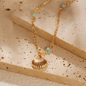 Détail d'un collier pendentif coquillage doré avec perles turquoise sur fond en pierre