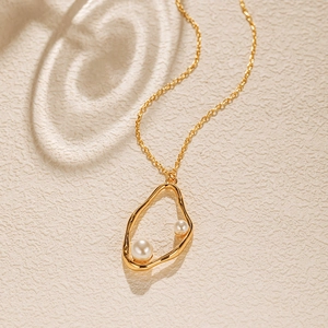 Détail du pendentif doré irrégulier avec deux perles sur une fine chaîne de collier