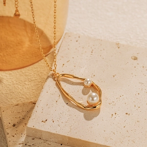 Détail d'un collier doré vintage avec pendentif ovale irrégulier et deux perles blanches