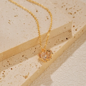 Détail du pendentif coeur avec zircon clair et filigrane doré sur fond de pierre