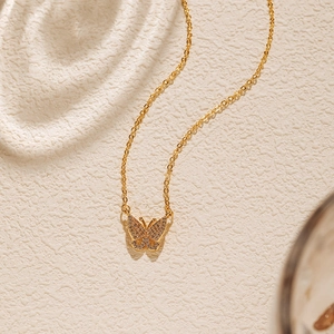 Détail du collier pendentif papillon doré avec zircons étincelants sur fond texturé fin
