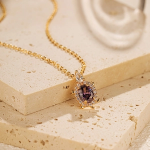 Détail du pendentif tortue dorée avec une pierre violette ovale et des zircons