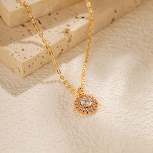 Détail d'un collier pendentif halo doré avec zircon posé sur une pierre naturelle beige