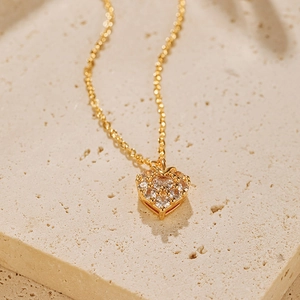 Vue macro du collier pendentif cœur doré avec des pierres de zircon sur surface en pierre