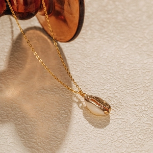 Détail d'un pendentif en cauris naturel avec placage à l'or sur une chaîne fine