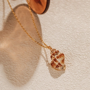 Gros plan d'un collier doré avec un pendentif en forme de conque aux motifs réalistes