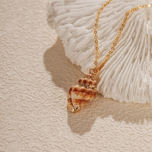 Vue macro d'un collier pendentif coquillage avec bordure dorée sur fond corail et sable