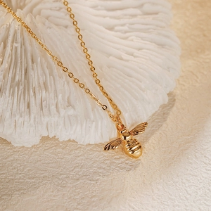 Gros plan d'un pendentif abeille doré sur une chaîne fine avec des ailes texturées