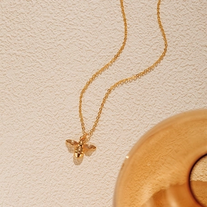 Gros plan du collier avec pendentif abeille dorée sur fond texturé avec lumière douce