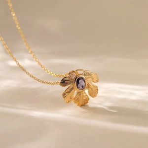 Macro della collana con pendente a foglia dorata e cristallo viola su tessuto beige