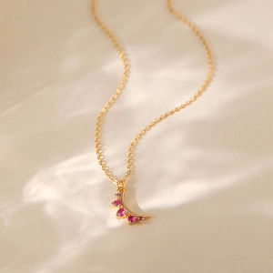 Dettaglio della collana a mezzaluna dorata con gemme rosa su sfondo con riflessi