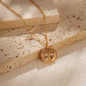 Détail d'un collier plaqué or avec pendentif papillon rond sur un support en pierre texturée