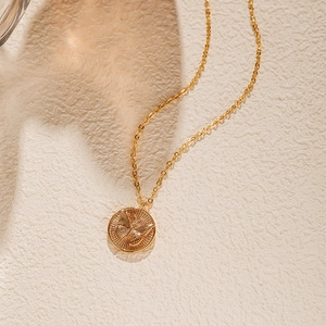 Détail d'un collier médaillon papillon doré sur un fond en pierre texturée