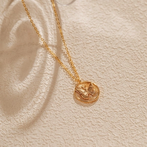 Détail d'un collier vintage doré avec médaillon rond gravé d'un motif de papillon